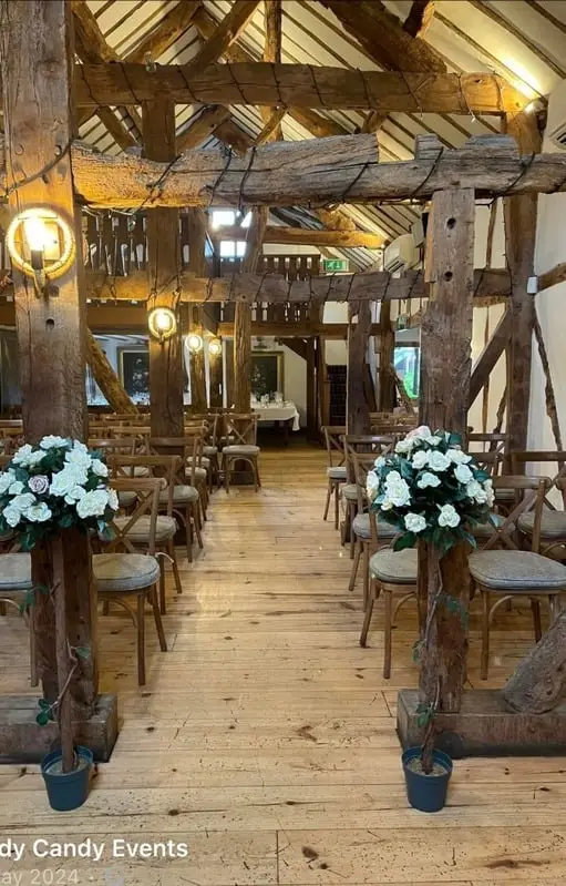 Beamed barn ceremony room with white floral arrangements lining the aisle