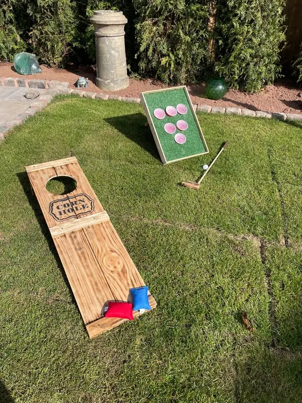 Wooden corn hole boards and a putting game set out on grass