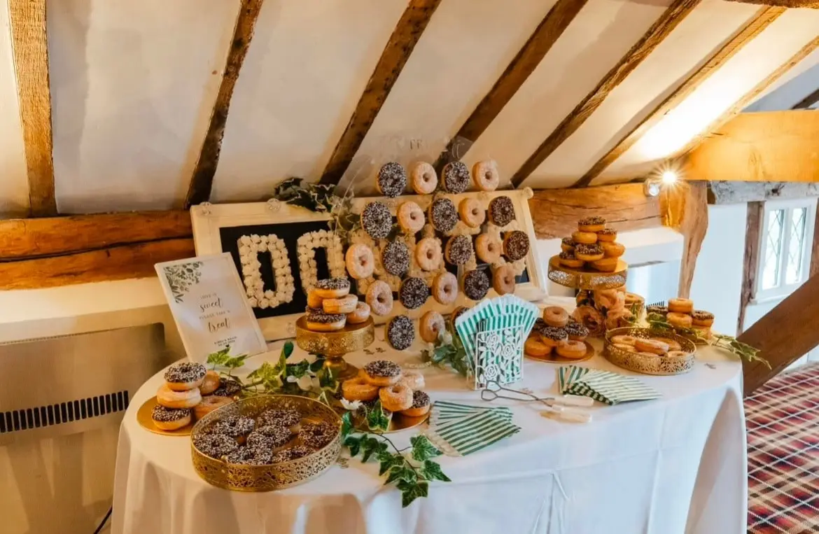 Donut display on a lace-covered table in a beamed barn, with foliage and donut bags