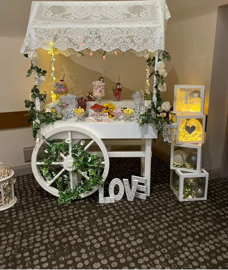 White sweet cart with illuminated LOVE blocks and balloons alongside
