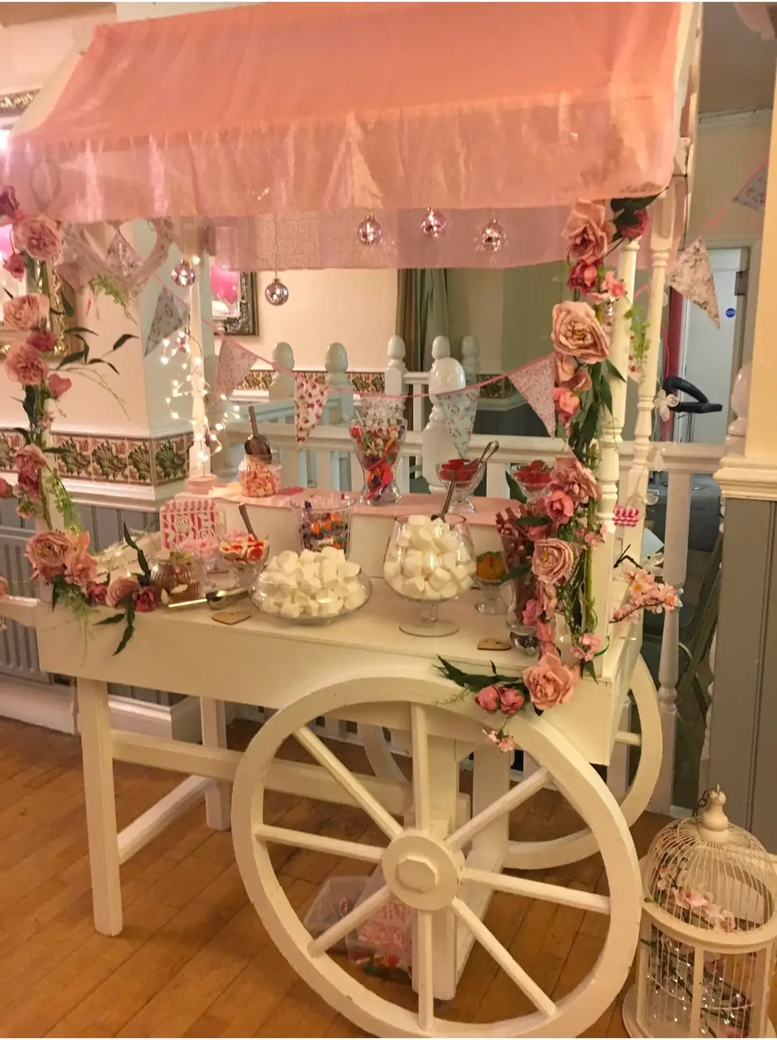 White wooden sweet cart filled with jars of sweets and dressed with peach and cream roses