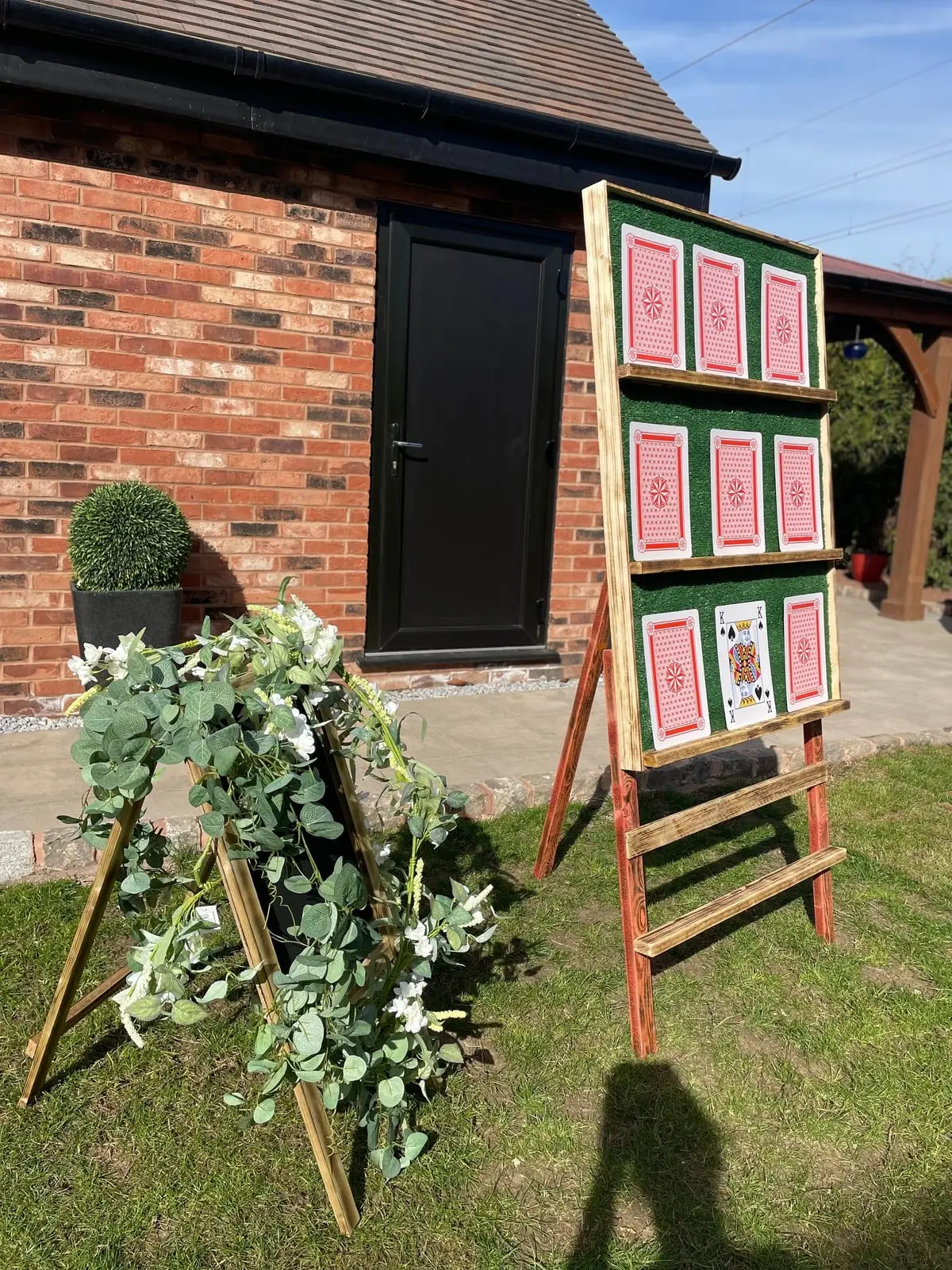 Wooden easel table plan framed by a green foliage arch outside a brick venue